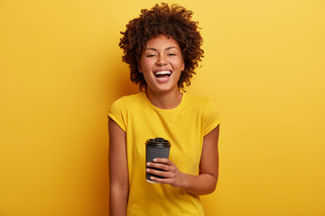 monchrome shot of cheerful dark skinned woman laughs and talks casually, holds disposable cup of tea