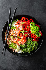 Canvas Print - poke bowl of brown rice, trout or salmon fillet, Chuka Seaweed Salad, sesame and fresh vegetables on dark background, top view, copy space, healthy food trend