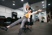 Happy Woman Pushing Colleague Sitting On Office Chair And Having Fun Time