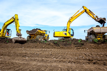 Big excavators are loading two trucks with ground on building site