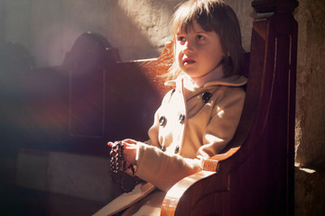 Portrait of little cute child girl praying in the church in in the rays of the sun. Faith, religion, prayer concept.