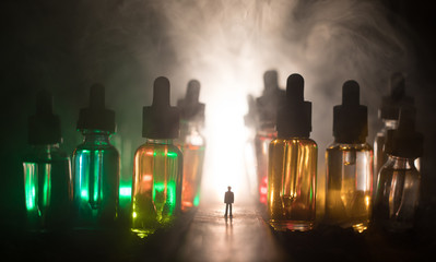 Silhouette of a man standing in the middle of the road on a misty night with giant glass bottles filled with electronic cigarette liquid. Colorful foggy clouds with light on background.