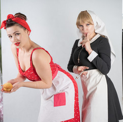 two cute girlfriends dressed up for a costume cosplay party. one girl is dressed as a housewife in pinup style, the second woman is dressed as a nun with a syringe. they stand on a white background.