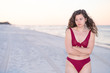 © Andriy Blokhin - Young woman cold shivering sad crossed arms in red bikini swimsuit standing in beach sunrise or sunset in Florida panhandle with calm ocean and sand