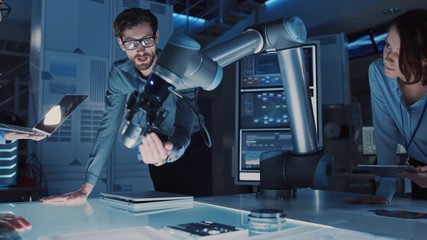 Leinwandbilder - Diverse Team of Engineers with Laptop and a Tablet Analyse and Discuss How a Futuristic Robotic Arm Works and Moves a Metal Object. They are in a High Tech Research Laboratory with Modern Equipment.