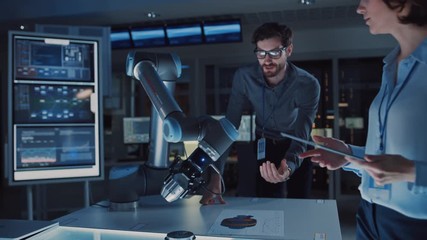 Leinwandbilder - Diverse Team of Engineers with Laptop and a Tablet Analyse and Discuss How a Futuristic Robotic Arm Works and Moves a Metal Object. They are in a High Tech Research Laboratory with Modern Equipment.