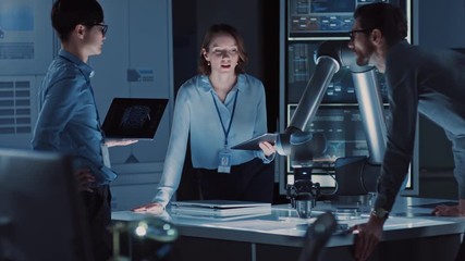 Leinwandbilder - Diverse Team of Engineers with Laptop and a Tablet Analyse and Discuss How a Futuristic Robotic Arm Works and Moves a Metal Object. They are in a High Tech Research Laboratory with Modern Equipment.