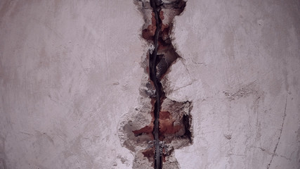 Background gray wall divides the middle of the groove with a black electric wire, in the groove visible red bricks, concrete 