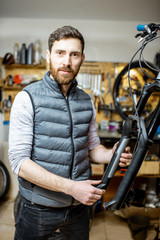 Wall Mural - Portrait of a handsome repairman serving a bicycle, fixing some malfunctions with bicycle fork at the workroom