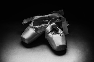 Wall Mural - Pointe shoes ballet dance shoes with a bow of ribbons beautifully folded on a dark background.
