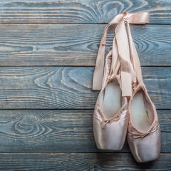 Wall Mural - Pointe shoes ballet dance shoes with a bow of ribbons hang on a nail on a wooden background.