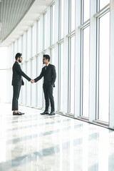 Two indian businessmen shaking hands standing at big window with urban cityscape, confident business partners handshaking in office, forming good relations, establish partnership, support, help. 