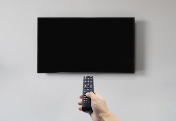 Television on white wall with hand using remote control, blank black screen