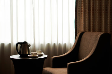 white tea cup coffee cup on the table by a sofa couch in hotel room, kettle