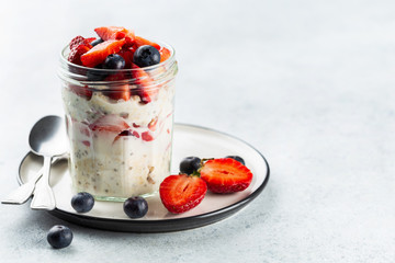 overnight oats with chia seeds and fresh strawberries and blueberries in a glass jar. healthy breakf