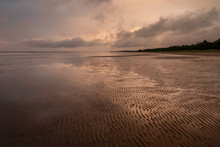 Calm Evening At The Seashore During Low Tide. Repetitive Lines In The Sand Going To Darkening Clouds In The Sky