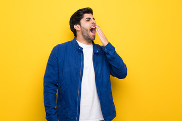 Wall Mural - Man with blue jacket over yellow wall yawning and covering wide open mouth with hand