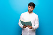 © luismolinero - Young man over isolated blue wall holding a book and enjoying reading
