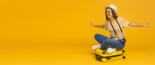 Horizontal Banner Of Young Tourist Girl Sitting On Suitcase, Pretending Flying On A Plane, Isolated On Yellow Background With Copy Space. Dreams About Traveling Concept