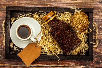 Wall Mural - White cup with black coffee and coffee grains on a wooden table background. View from above. Place for text.