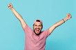 Successful caucasian male holding hands up, achieves cherished goal, looks excited and amazed, feels triumph, screams with happiness, has overjoyed expression, isolated over pink background.