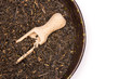 Lot of pieces of dry black tea earl grey in a grey ceramic bowl with wooden scoop flatlay isolated on white background