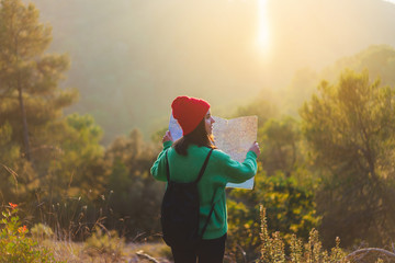 Back view of happy smiling traveller girl holding a map and enjoying a trip in the forest