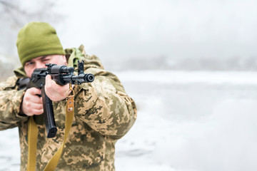 A soldier with a gun in camouflage holds a weapon in his hands and directs him forward.