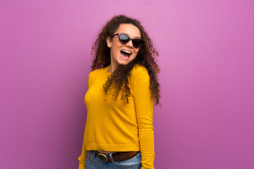 Teenager girl over purple wall with glasses and smiling