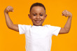 Leinwandbild Motiv Handsome confident Afro American eight year old child in casual t-shirt smiling happily and raising clenched fists, tensing muscles, feeling strong and full of energy after ate healthy protein lunch