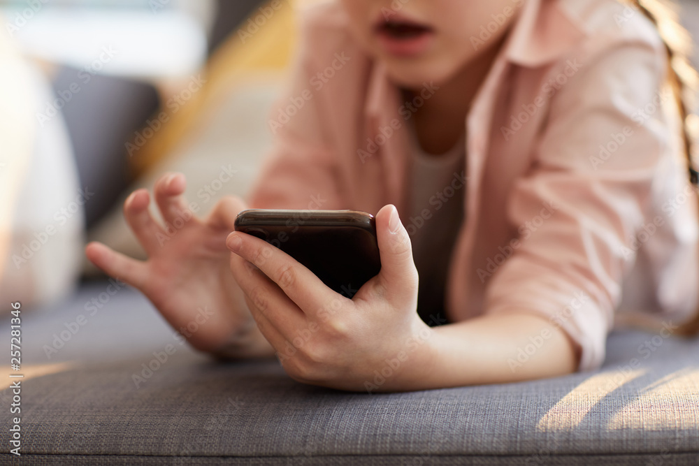 Closeup of unrecognizable little girl using smartphone, focus on hands scrolling through internet, copy space