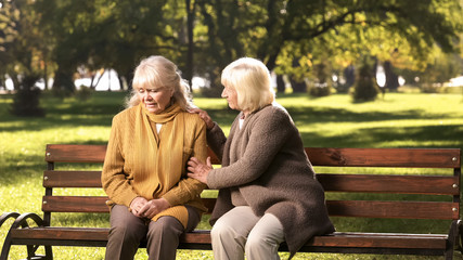 Senior lady comforting old friend about her loss, sitting on bench in park