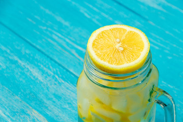 Water with lemon. Lemonade with lemon slices on blue wooden background.