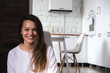 © ILIA - Young smiling woman sitting on the floor in the living room opposite the kitchen