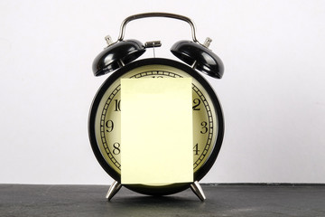 Black alarm clock on the wooden surface and yellow sticker over white.