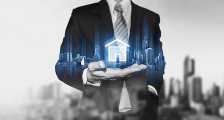 Wall Mural - Businessman holding modern buildings hologram, and home icon. Real estate business, building technology and smart home concept