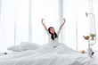 © Nattakorn - Asian woman wake up in the morning, sitting on white bed and stretching, feeling happy and fresh