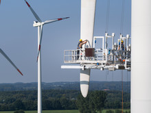 Workers On A Hanging Platform Repair A Damaged Rotor Blade On A Wind Turbine