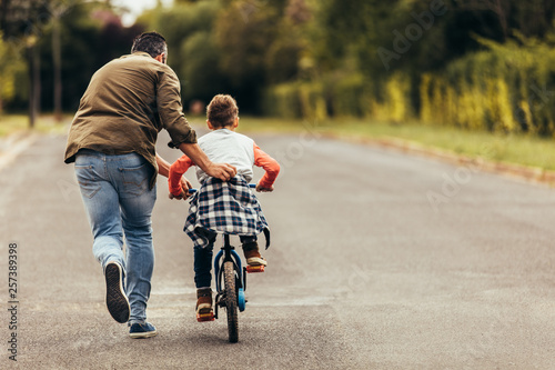 Cuadros en Lienzo Man helping his kid in learning to ride a bicycle