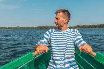 Young man rowing boat through lake in summertime