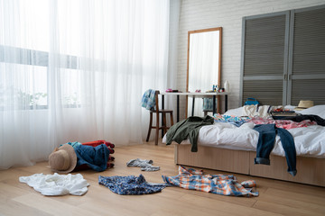 straw hat and colorful clothes in luggage on wooden floor. empty nobody in messy white bed in bedroo