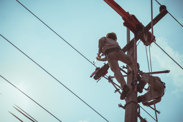 Two linemans use devices that are insulated for maintenance high voltage distribution system. To prevent power outages. The background is the sky.