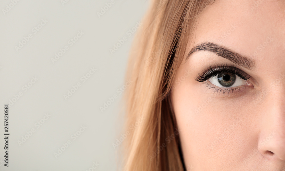Young woman with beautiful eyelashes on light background, closeup