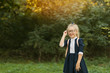 © oes - Little happy smiling smart girl in glasses and uniform standing in the backyard of the school. schoolgirl goes to first grade. Copy space for text on left side