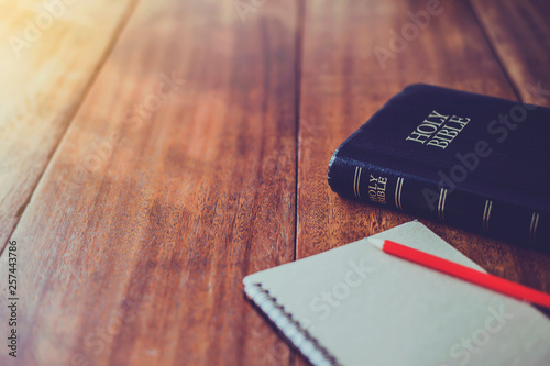 Fotomural Holy bible with note book and pencil on wooden table against morning sun light