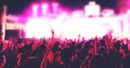 blurry of silhouettes of concert crowd at Rear view of festival crowd raising their hands on bright stage lights