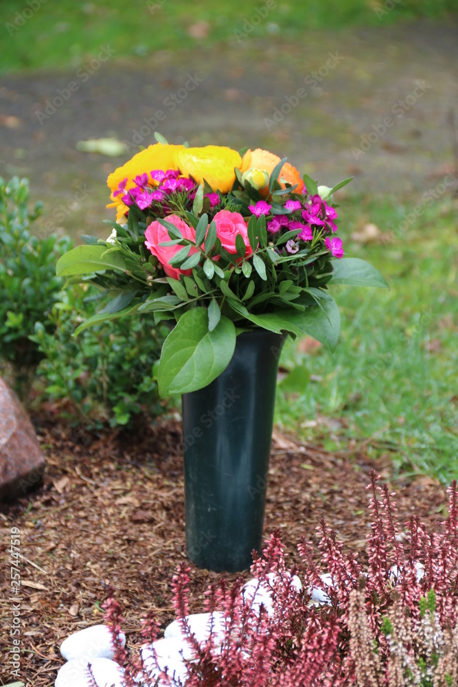 Stock-Foto „Bunte Blumen in Friedhofsvase schmücken ein Grab auf dem Friedhof“