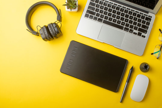 Desktop designer, and creative retoucher with a graphics tablet, laptop, glasses. Design, flat lay. On a yellow background