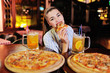 © Evgeniy Kalinovskiy - a young pretty girl eating pizza and drinking beer or a beer citrus cocktail on the background of a bar or pizzeria.