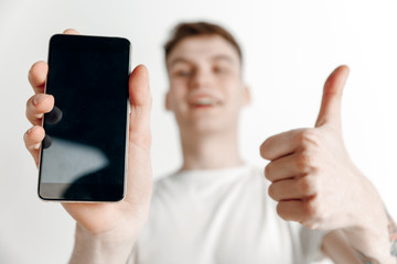 Its cool. Good news. Do that like me. Young handsome man showing smartphone screen and signing OK sign isolated on gray background. Human emotions, facial expression, advertising concept.